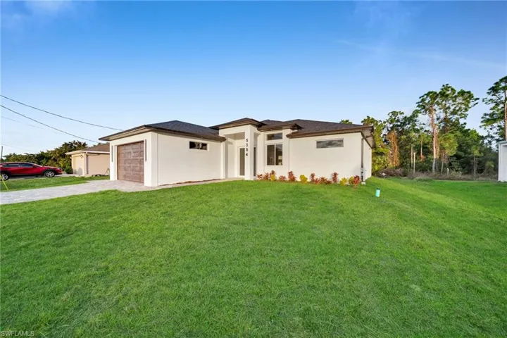Prairie-style home with a front yard, driveway, an attached garage, and stucco siding