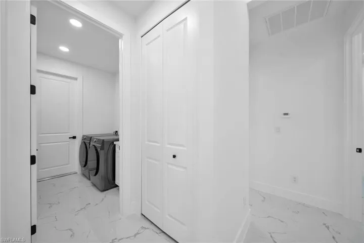 Laundry room with recessed lighting, light marble finish floors, and washer and clothes dryer