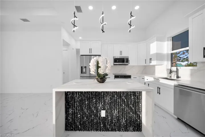 Kitchen with stainless steel appliances, light stone counters, white cabinetry, a kitchen island, and recessed lighting
