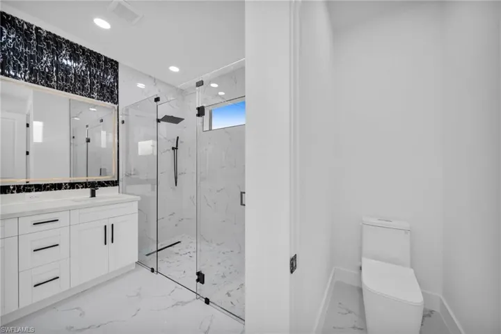 Bathroom featuring recessed lighting, a marble finish shower, vanity, and marble tiled flooring