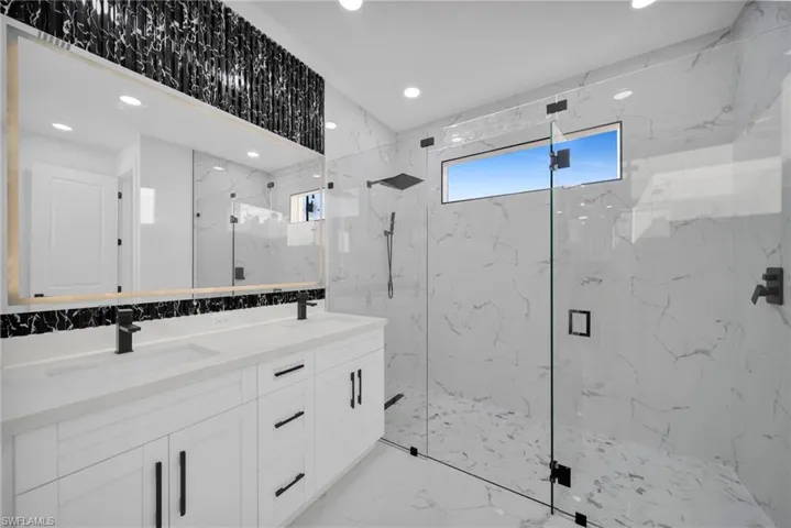 Bathroom with stone wall, recessed lighting, double vanity, a marble finish shower, and light marble finish floors