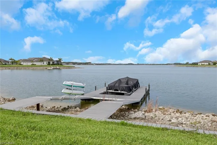 Lakefront property featuring a private dock with boat lift and kayak storage, extensive water frontage, and lush green lawn