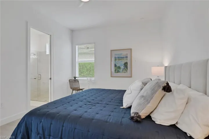 Bedroom featuring a built-in upholstered headboard, a window with horizontal blinds, and a door frame providing access to a glass-enclosed shower