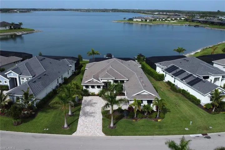 Waterfront property featuring a paver driveway, mature palm trees, tile roofing, and manicured landscaping
