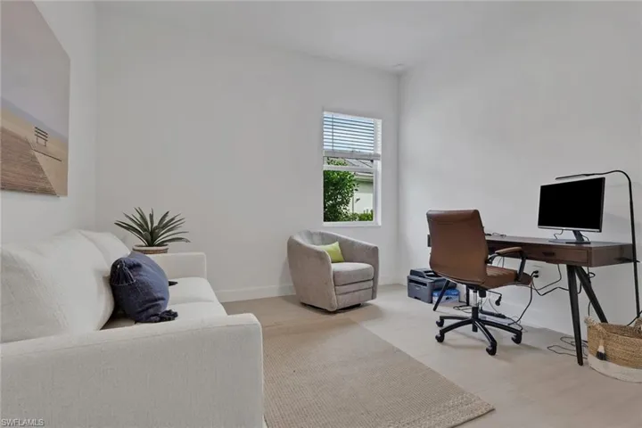 Bright interior space with light wood-finish flooring, white walls, and a window featuring blinds