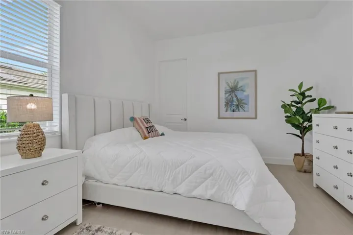 White-painted interior room featuring light wood-finish flooring, a window with horizontal blinds, a white door, and a framed art piece