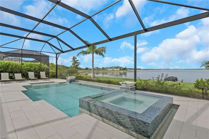 Screened-in outdoor living space featuring a pool and integrated spa with mosaic tile surround, spacious paver patio, and mature landscaping