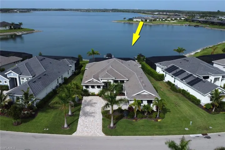 Waterfront property featuring a paver driveway, mature palm trees, tile roof, and manicured lawn