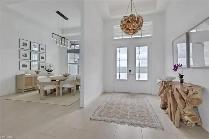 Foyer with double entry doors and transom window, featuring a decorative chandelier and light wood-finish flooring
