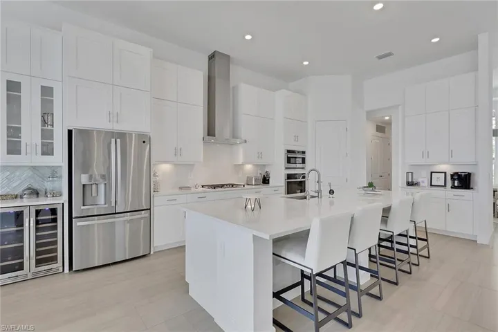 Spacious kitchen featuring white cabinetry, stainless steel appliances, a large center island with seating, recessed lighting, and light wood-finish flooring