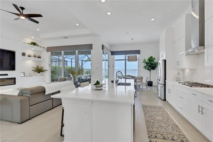 Open-concept living space featuring a modern kitchen with white cabinetry and stainless steel appliances, a center island with a sink, light wood-finish flooring, and recessed lighting