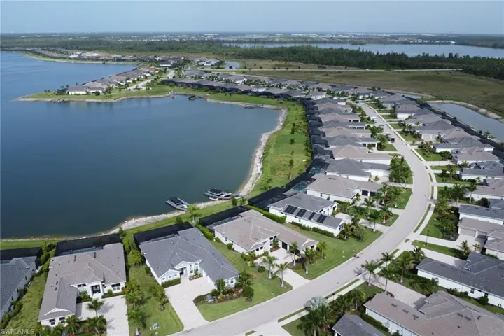 Aerial perspective of a lakeside residential community featuring a curved street, uniform home designs, and verdant landscaping