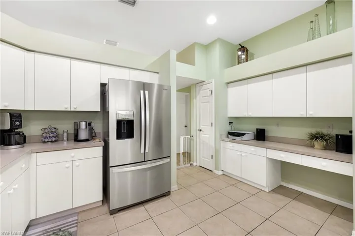 Kitchen featuring white cabinetry, built in desk, light tile patterned floors, and stainless steel refrigerator with ice dispenser