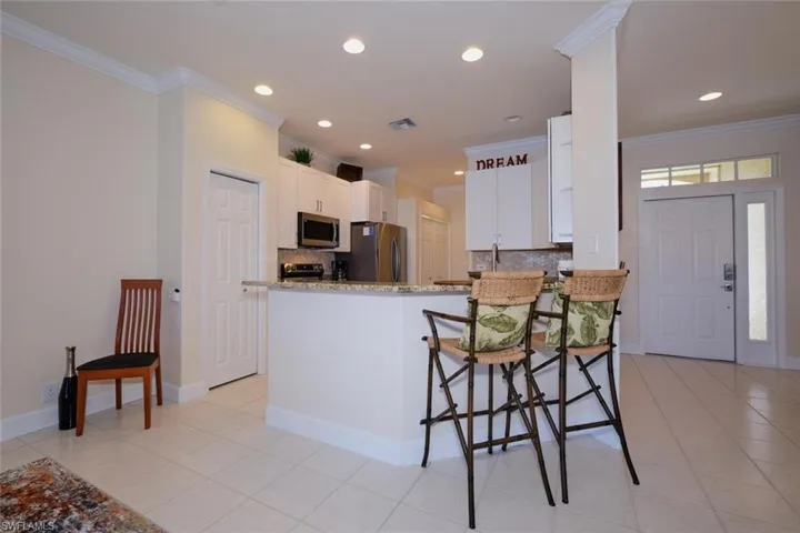 Kitchen featuring backsplash, white cabinetry, light stone countertops, a peninsula, and a breakfast bar area