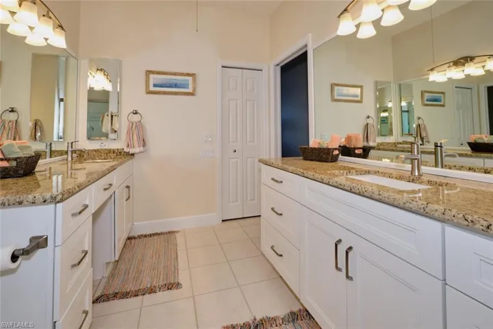 Full bathroom with two vanities, light tile patterned floors, and a closet