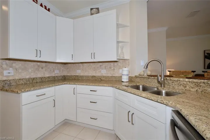 Kitchen featuring open shelves, crown molding, white cabinets, light stone counters, and decorative backsplash