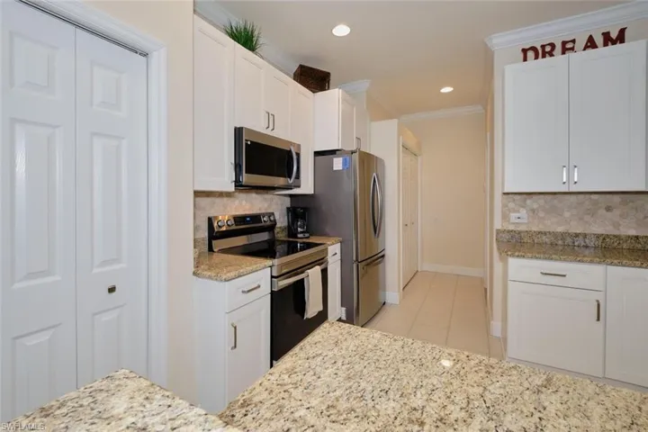 Kitchen with tasteful backsplash, stainless steel appliances, white cabinetry, light stone counters, and crown molding