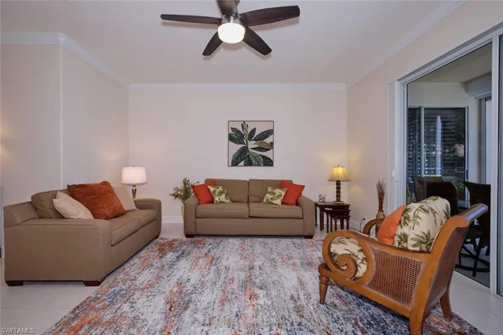 Living area with light tile patterned flooring, ceiling fan, and crown molding