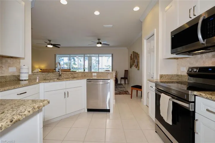 Kitchen with stainless steel appliances, backsplash, a peninsula, white cabinetry, and ornamental molding