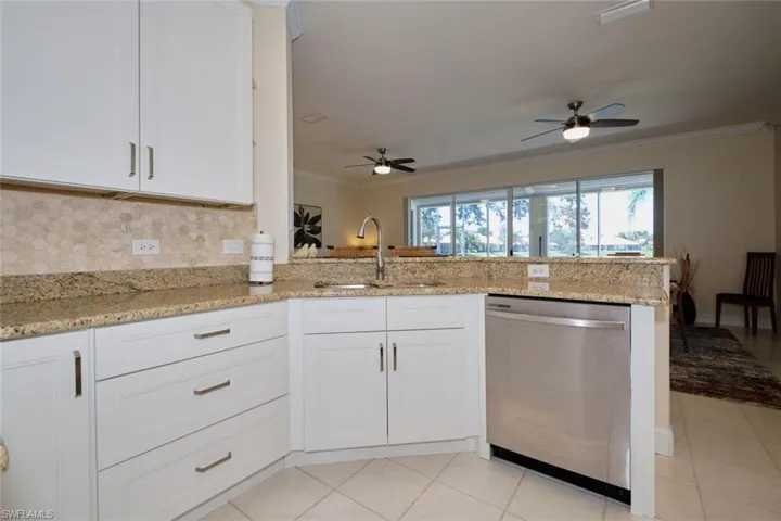 Kitchen with a peninsula, stainless steel dishwasher, white cabinets, light stone countertops, and ornamental molding