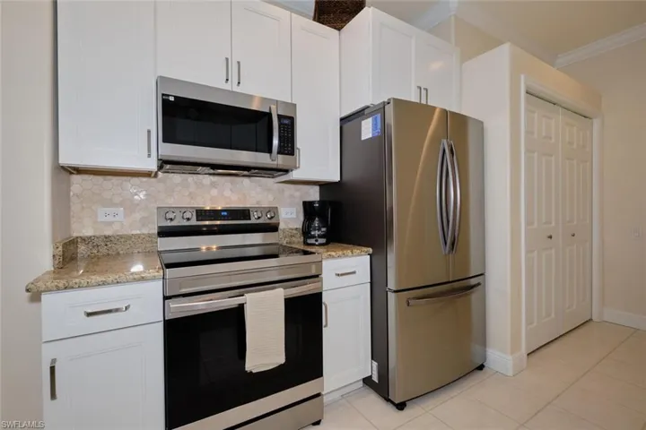 Kitchen with stainless steel appliances, white cabinets, light stone counters, and crown molding