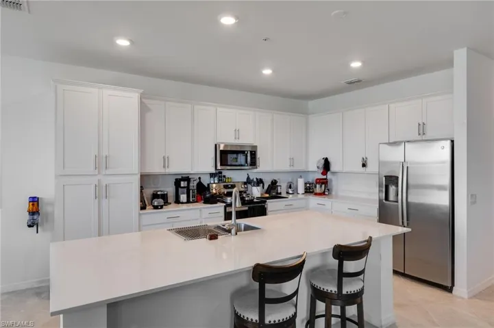 Kitchen featuring stainless steel appliances, white cabinets, a kitchen bar, a kitchen island with sink, and recessed lighting