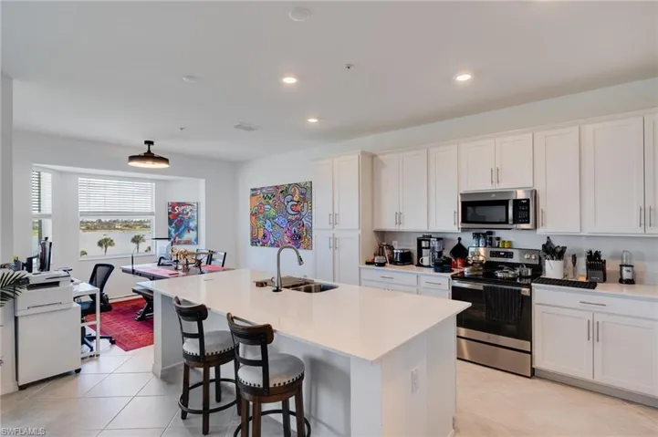 Kitchen with stainless steel appliances, white cabinets, a center island with sink, a kitchen bar, and recessed lighting