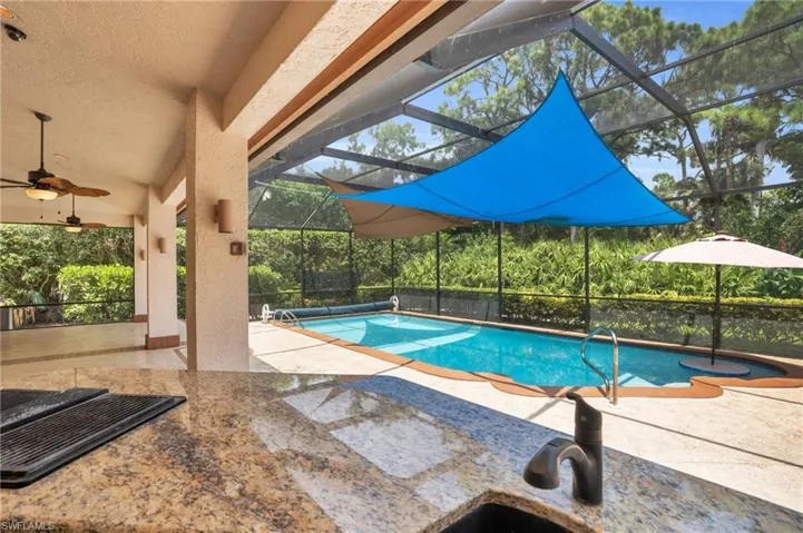 Poolside view featuring ceiling fan, lanai, and tropical landscaping