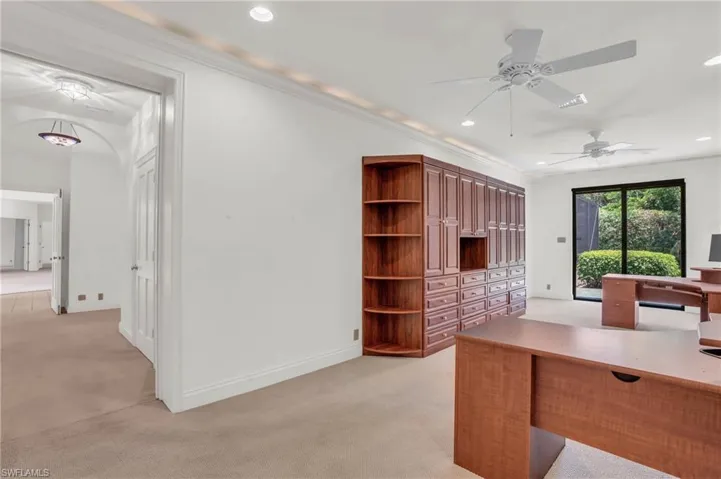 Carpeted office space with built-in shelving and ceiling fan