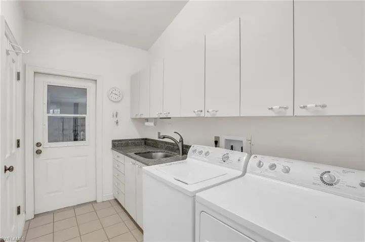 Clothes washing area featuring sink, washing machine and dryer, light tile patterned floors, and cabinets