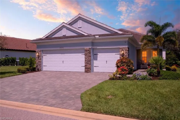 Stucco exterior featuring stacked stone accents, a tile roof, and a paver driveway
