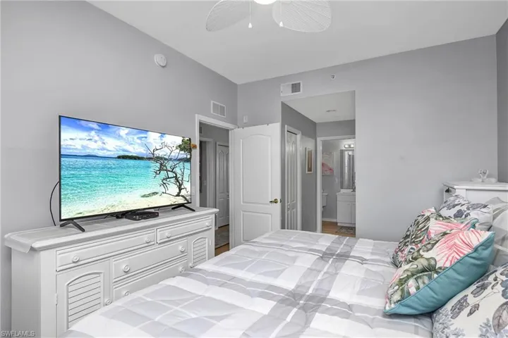 Bedroom with lofted ceiling, ensuite bath, visible vents, and a ceiling fan