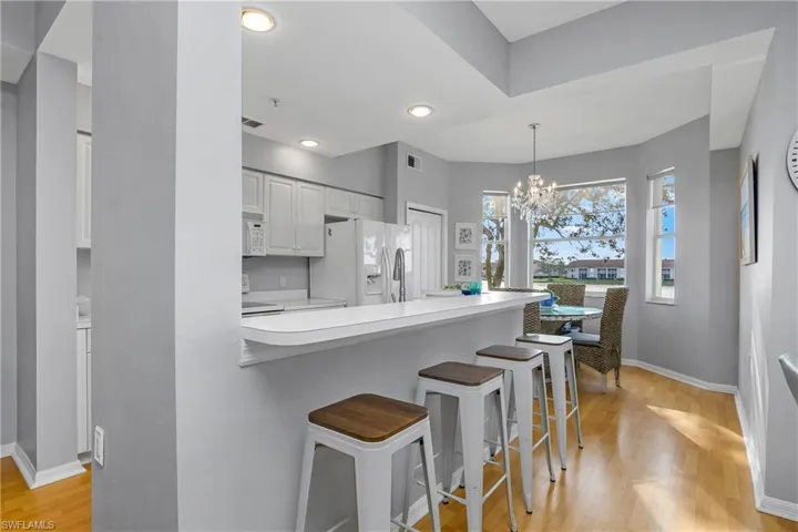 Kitchen with decorative light fixtures, light countertops, white cabinetry, light wood-type flooring, and white appliances