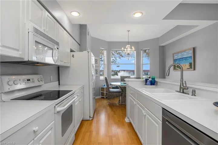 Kitchen featuring white appliances, white cabinets, hanging light fixtures, light countertops, and a sink