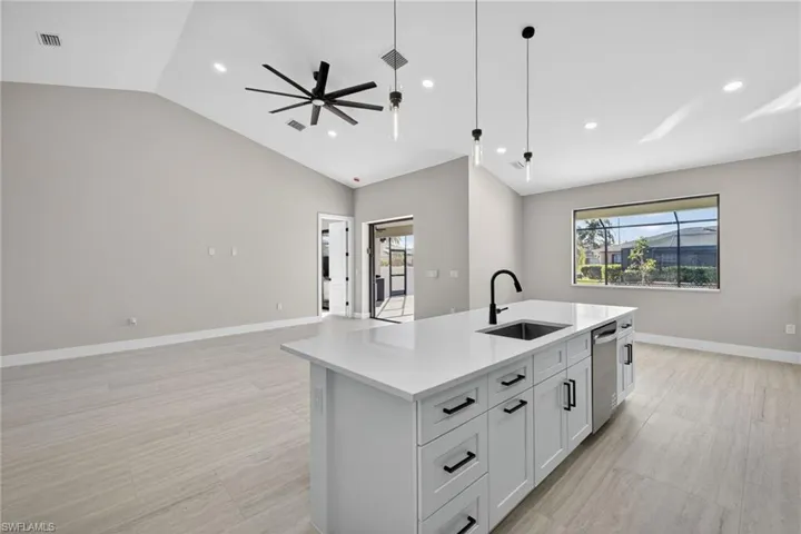 Kitchen featuring white cabinets, hanging light fixtures, lofted ceiling, an island with sink, and open floor plan