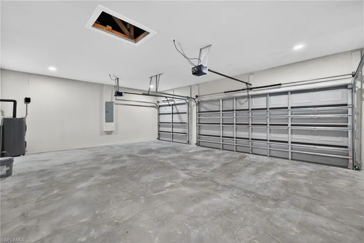 Garage with electric water heater, electric panel, recessed lighting, and a garage door opener