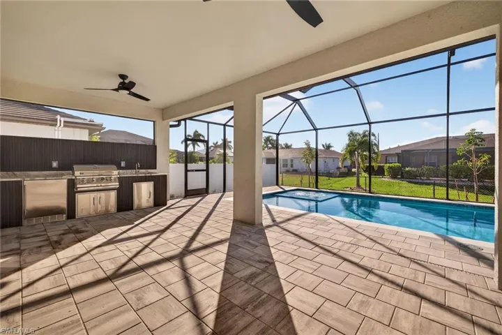 Swimming pool featuring an outdoor kitchen, a sunroom, a patio, and glass enclosure