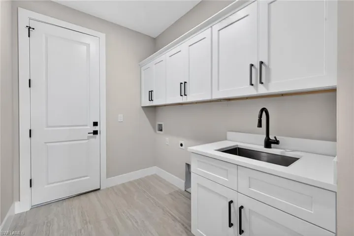 Washroom with electric dryer hookup, cabinet space, washer hookup, and light wood-style flooring