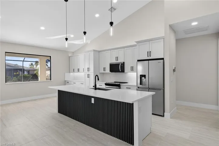 Kitchen featuring stainless steel appliances, decorative light fixtures, an island with sink, recessed lighting, and white cabinets