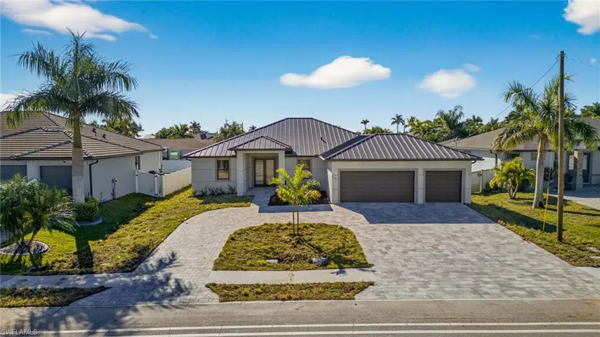 View of front of house featuring decorative driveway, stucco siding, a garage, and a metal roof
