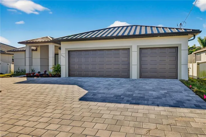 View of front facade featuring stucco siding, a standing seam roof, decorative driveway, a metal roof, and an attached garage