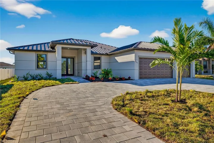 Prairie-style home featuring a standing seam roof, decorative driveway, stucco siding, and a metal roof