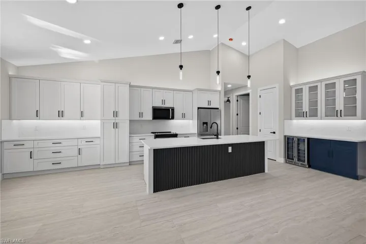 Kitchen with a center island with sink, high vaulted ceiling, hanging light fixtures, beverage cooler, and glass insert cabinets