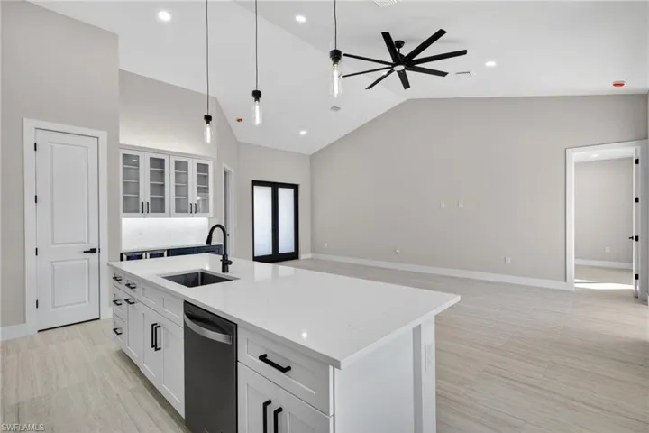 Kitchen with glass insert cabinets, a center island with sink, white cabinetry, light stone countertops, and recessed lighting