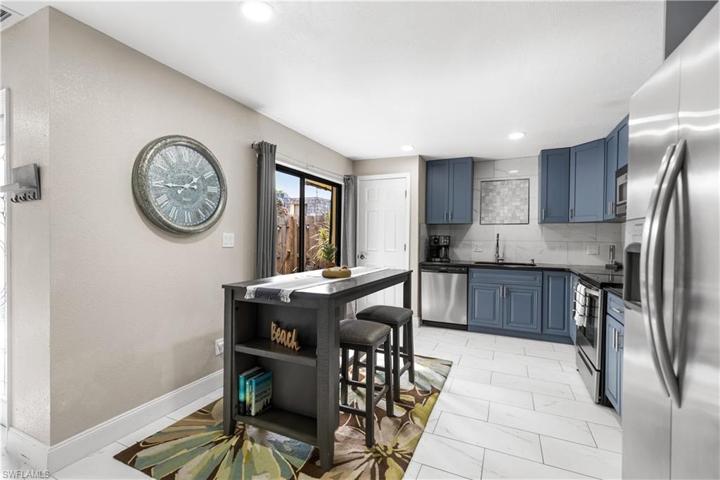 Kitchen with blue cabinetry, stainless steel appliances, custom mosaic tile feature above sink, high profile baseboards.