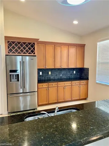 Kitchen with high end refrigerator, lofted ceiling, dark stone counters, wood finish cabinets, and backsplash