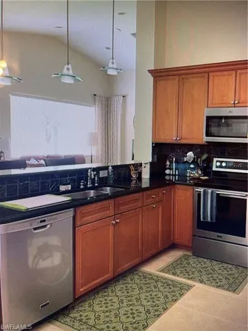 Kitchen with stainless steel appliances, decorative light fixtures, wood finish cabinets, lofted ceiling, and light tile patterned flooring