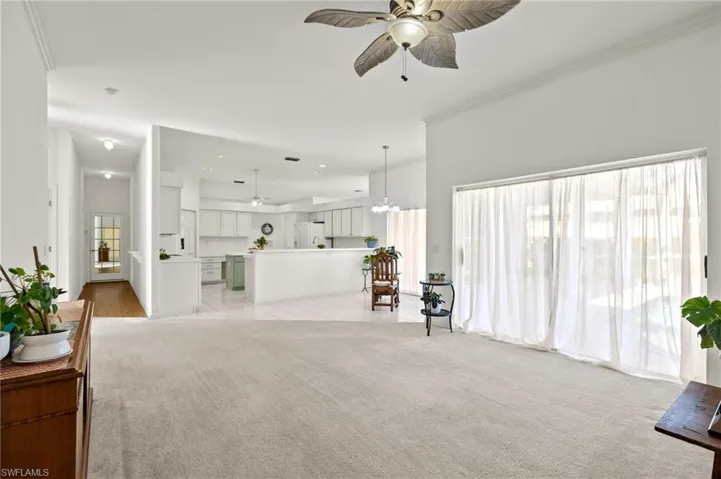 Carpeted living room with crown molding and ceiling fan with notable chandelier