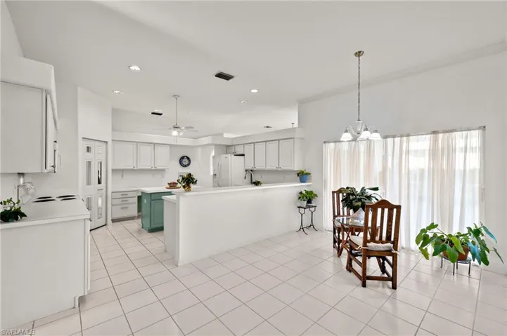 Kitchen with ceiling fan with notable chandelier, white refrigerator with ice dispenser, light tile flooring, and pendant lighting