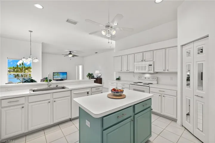 Kitchen with decorative light fixtures, a kitchen island, white cabinets, sink, and white appliances